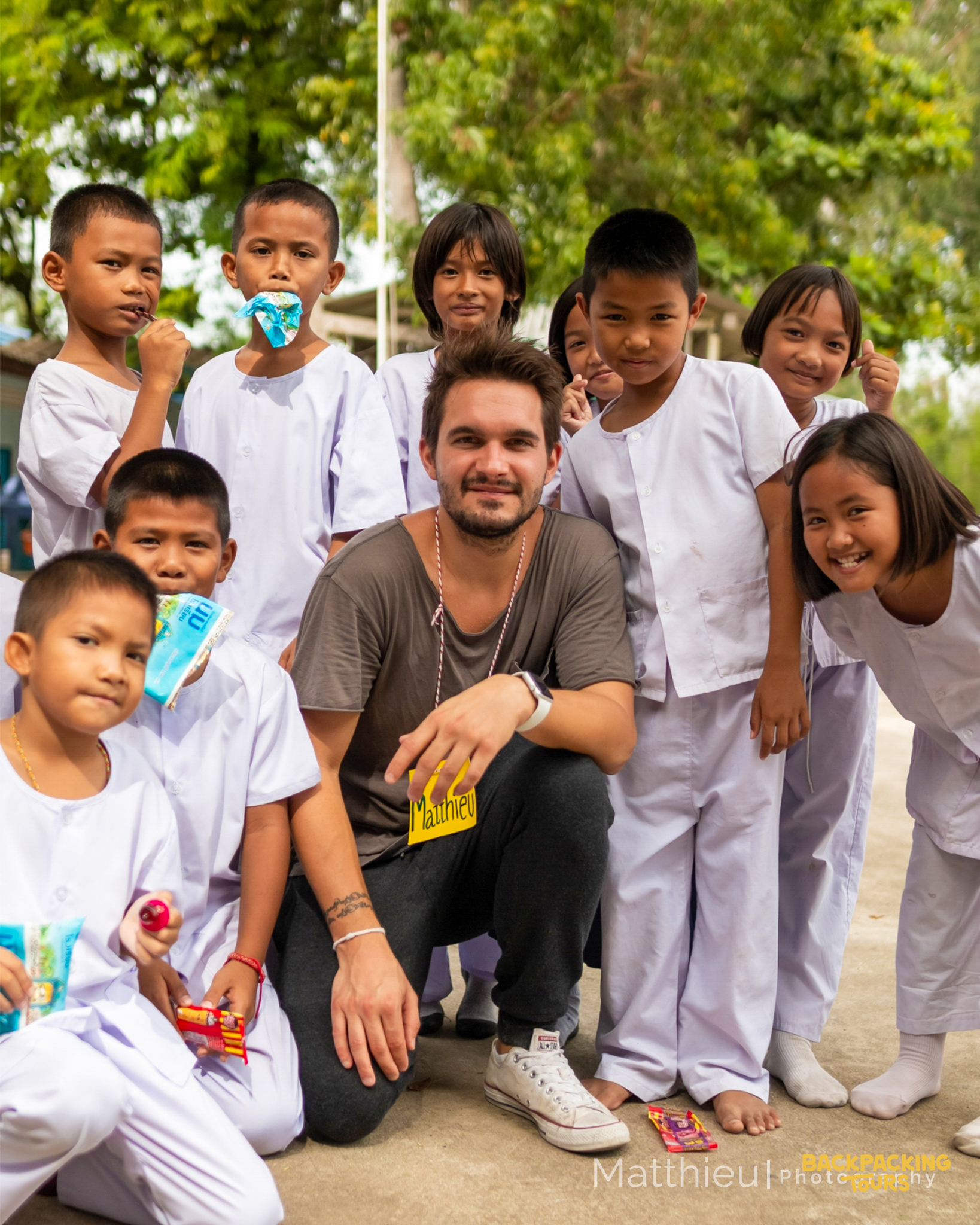 A friendly volunteer poses with a group of smiling children in white uniforms in Thailand.