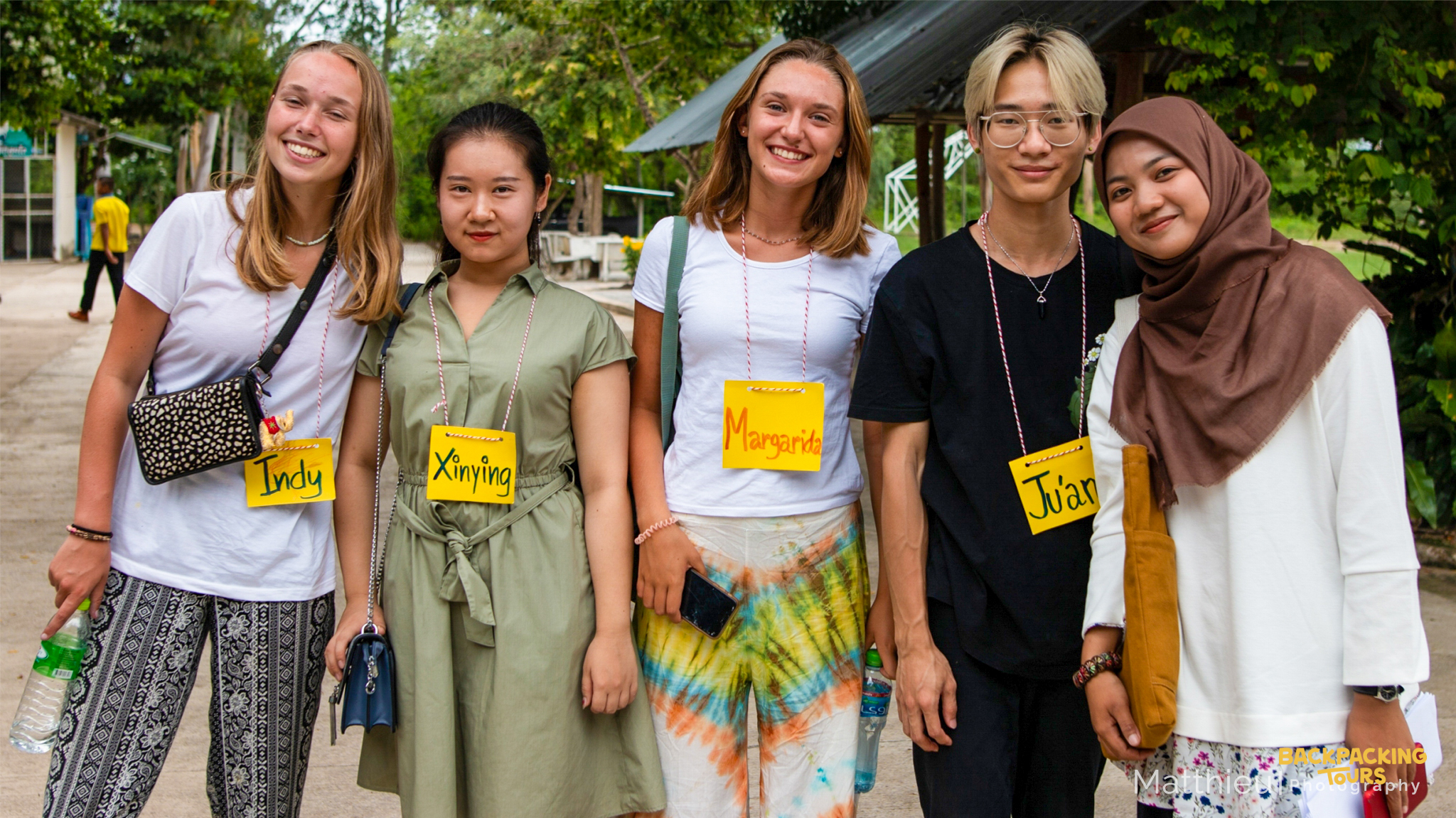 Smiling international volunteers wearing name tags stand together outdoors in Thailand.