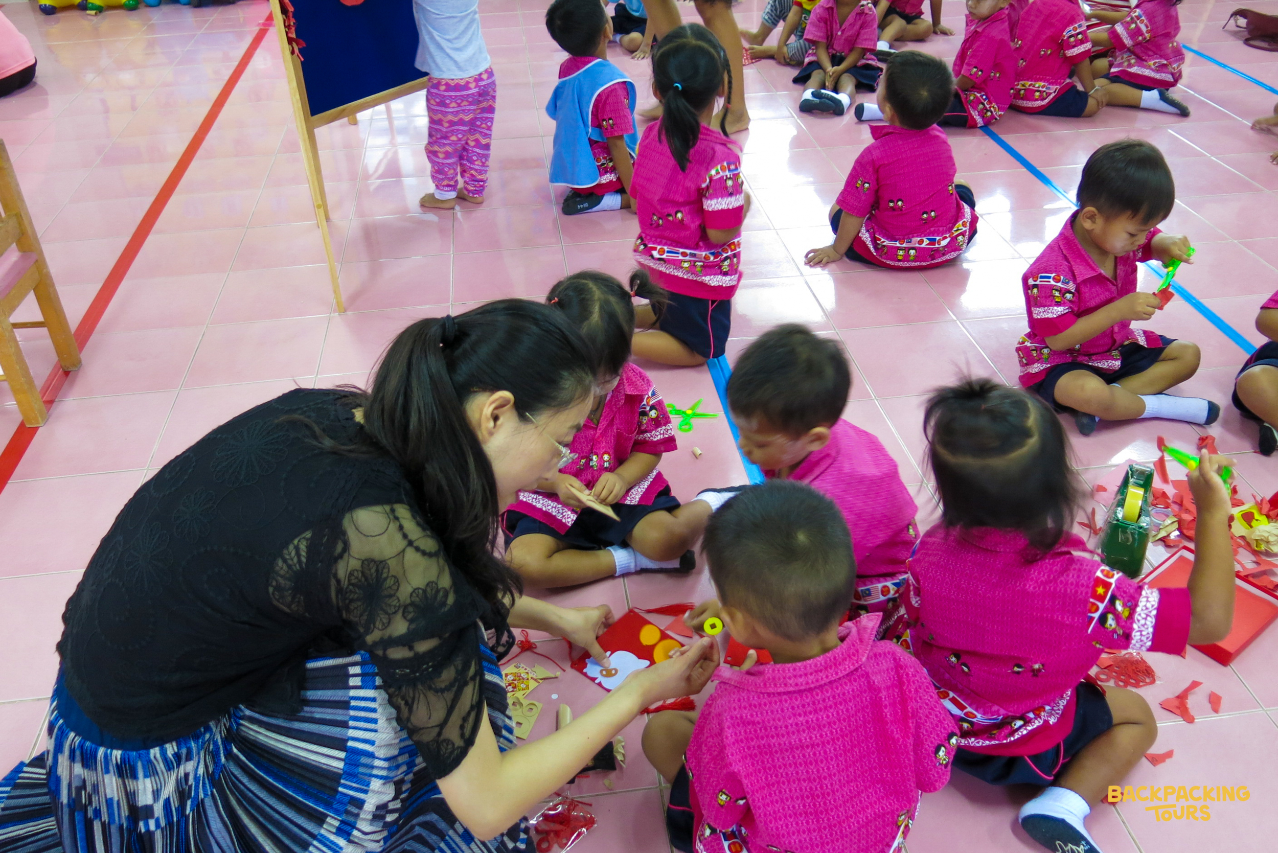 A volunteer helps young children in matching pink shirts with a craft activity in a Thai kindergarten.