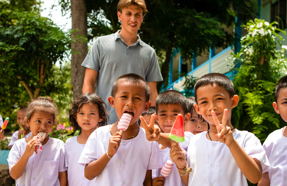 Joyful children in Thailand eat popsicles and make peace signs with a smiling volunteer.