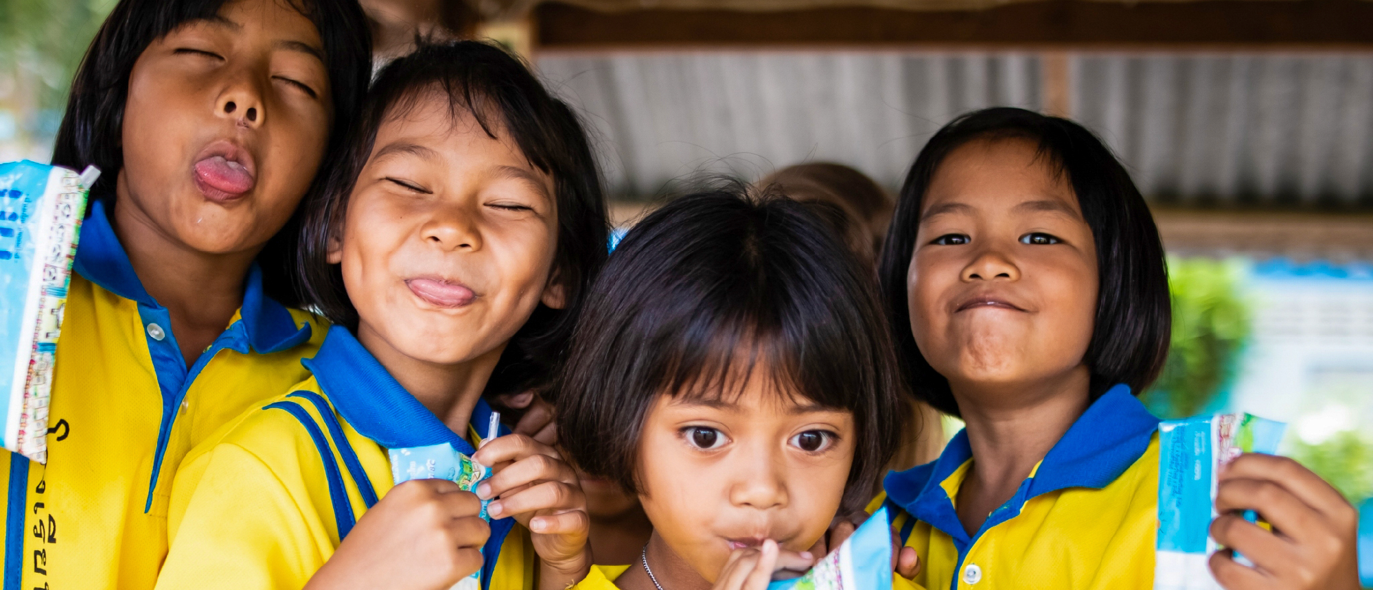 Four cheerful Thai students in yellow uniforms making funny faces while holding milk cartons.