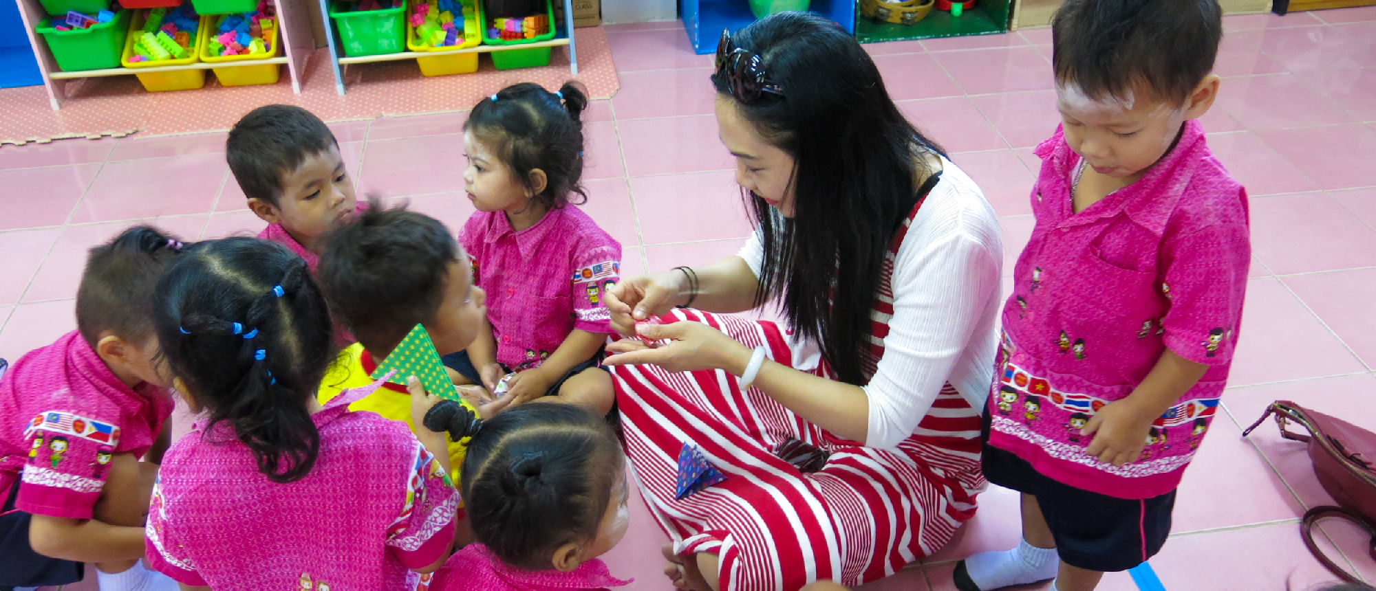 A volunteer teacher sits on the floor, engaging with young children in a Thai kindergarten.