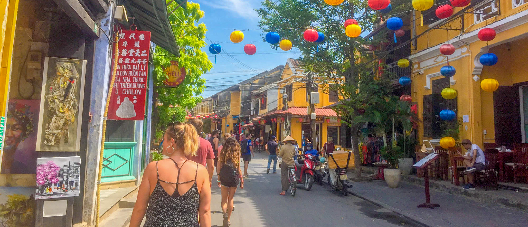 People explore a vibrant street in Hoi An, adorned with colorful lanterns and yellow buildings.
