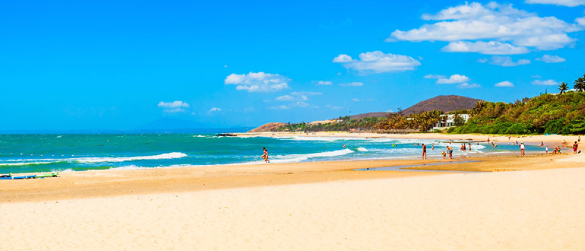 People enjoy the sunny sandy beach and turquoise ocean waves at Mui Ne, Vietnam.
