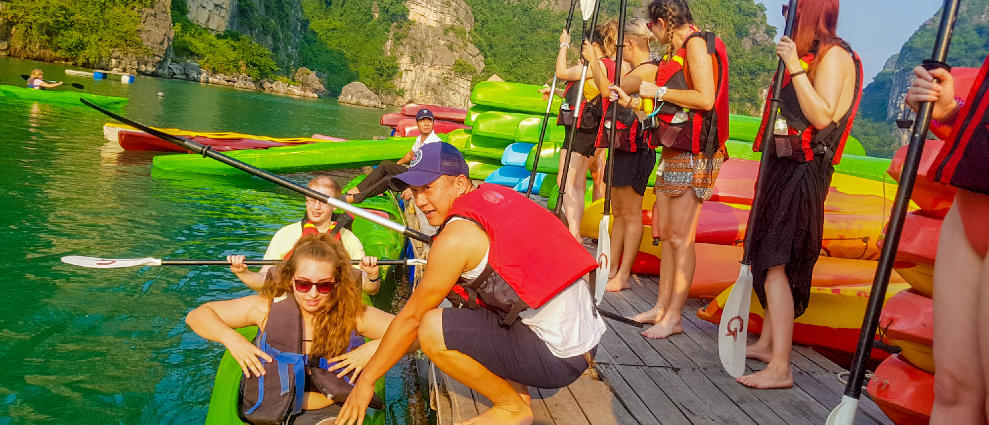 Travelers in life vests prepare to kayak on calm green water surrounded by karsts in Tam Coc, Vietnam.