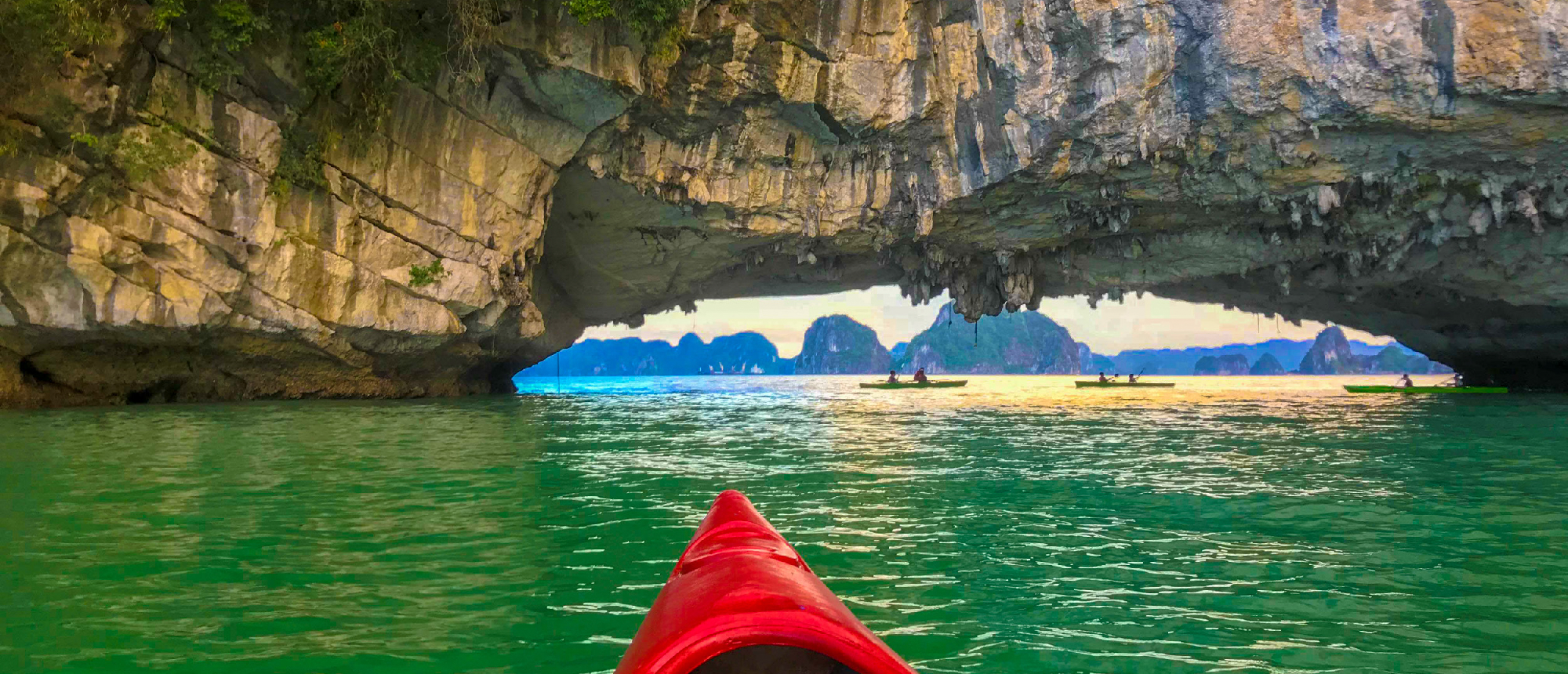 Kayaking through a majestic rock archway in the emerald waters of Halong Bay, Vietnam.