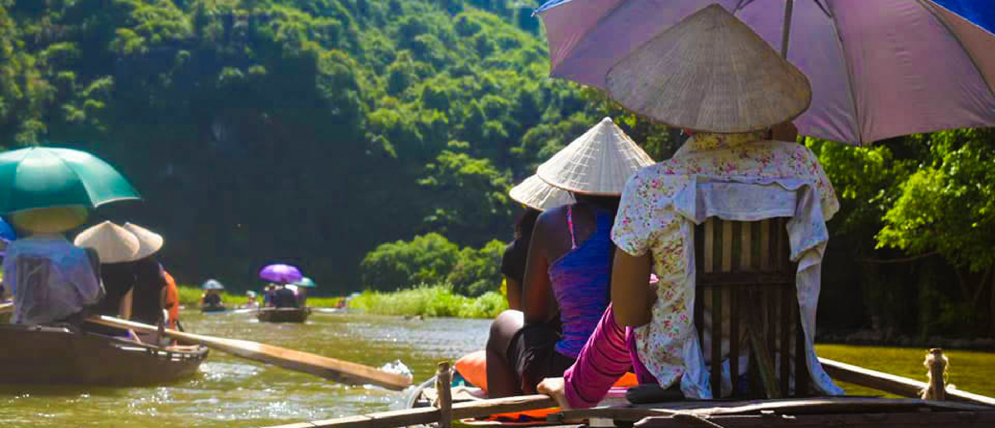 People in traditional conical hats on a sampan boat tour through scenic Tam Coc, Vietnam.