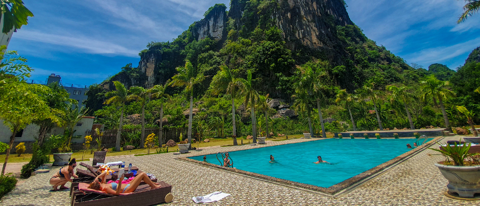 People swim and sunbathe in a pool surrounded by dramatic karst mountains in Phong Nha, Vietnam.