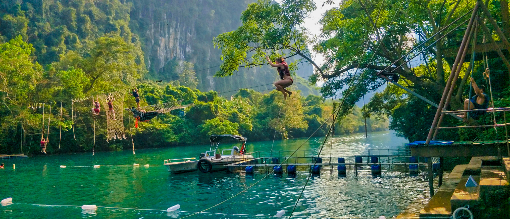 Adventurous travelers swing from a tree and navigate an obstacle course over the turquoise river in Phong Nha.