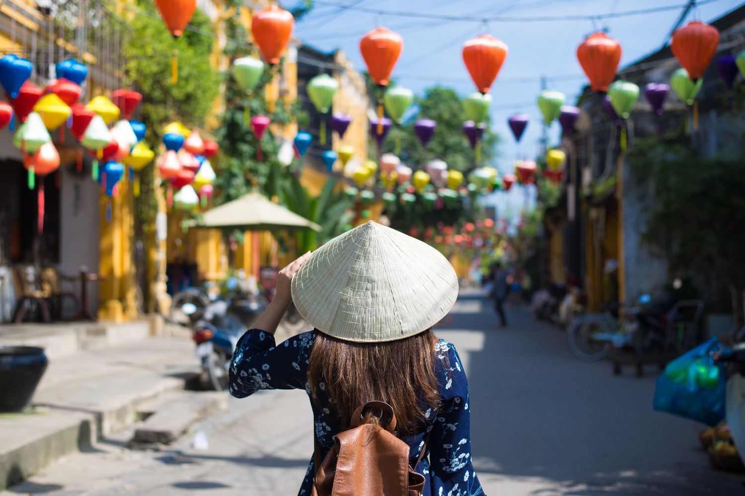 Woman in a conical hat exploring a vibrant Vietnamese street adorned with colourful lanterns.