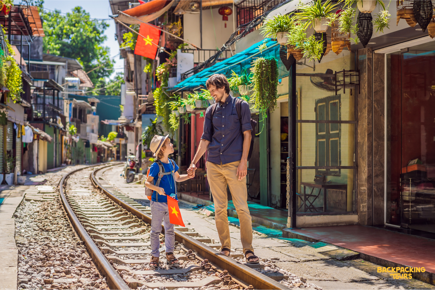 A father and son smile, holding hands on the railway tracks of a bustling Hanoi street.