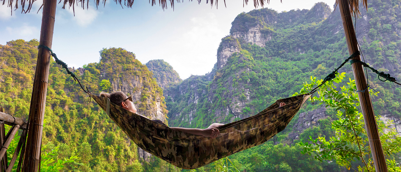 A person relaxes in a hammock overlooking the stunning limestone karsts of Ninh Binh, Vietnam.