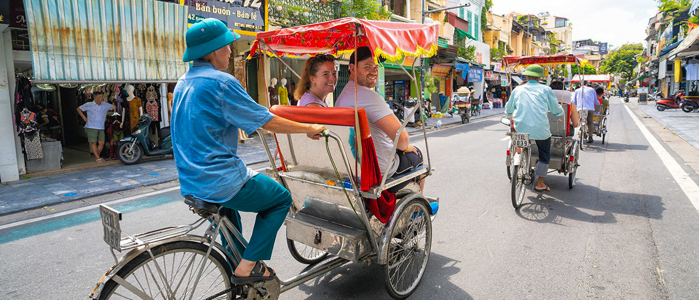 Two travelers experience a traditional cyclo ride through the lively Old Quarter of Hanoi.