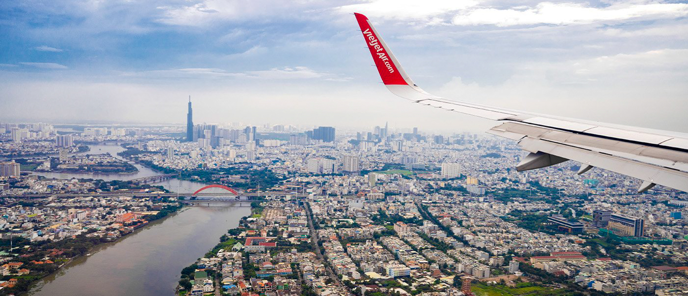 An airplane wing overlooks the sprawling Ho Chi Minh City with its river, bridges, and tall skyscrapers.