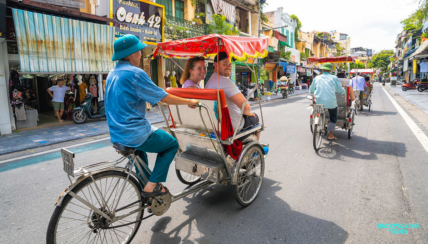 Two tourists enjoy a traditional rickshaw ride through the bustling streets of Hanoi.