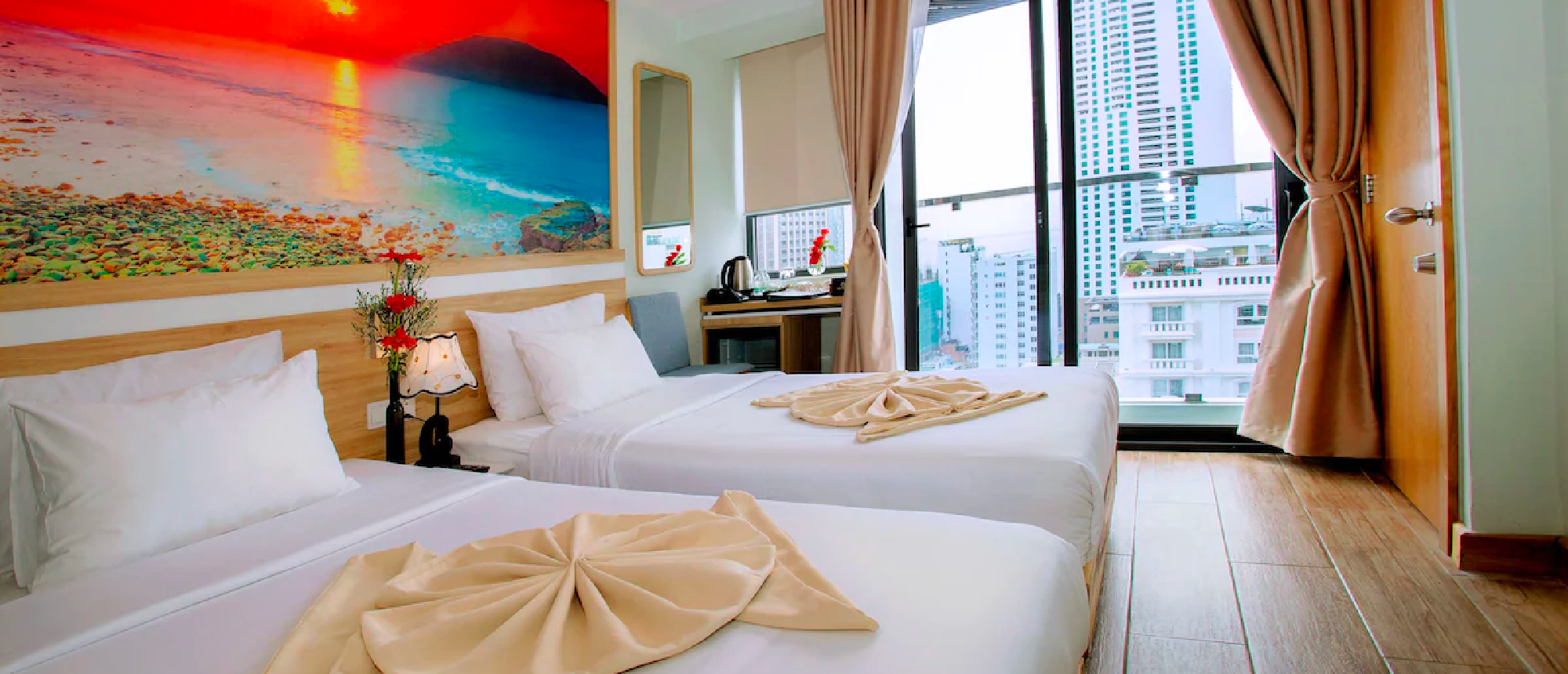 A modern hotel room in Nha Trang with two comfortable beds, beach art, and a city view.