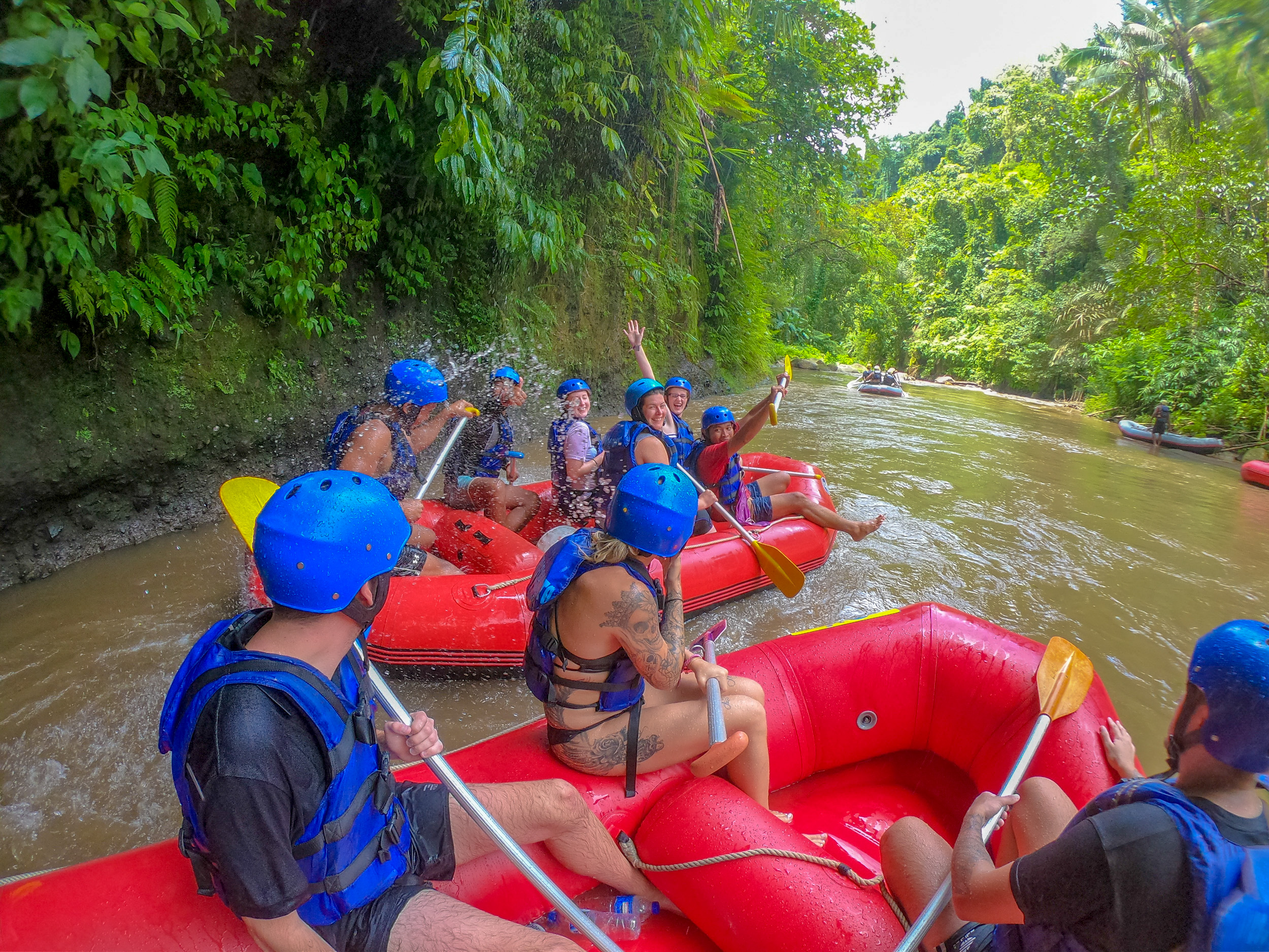 Adventurous backpackers rafting down a muddy river through lush green jungle in Bali, having fun.