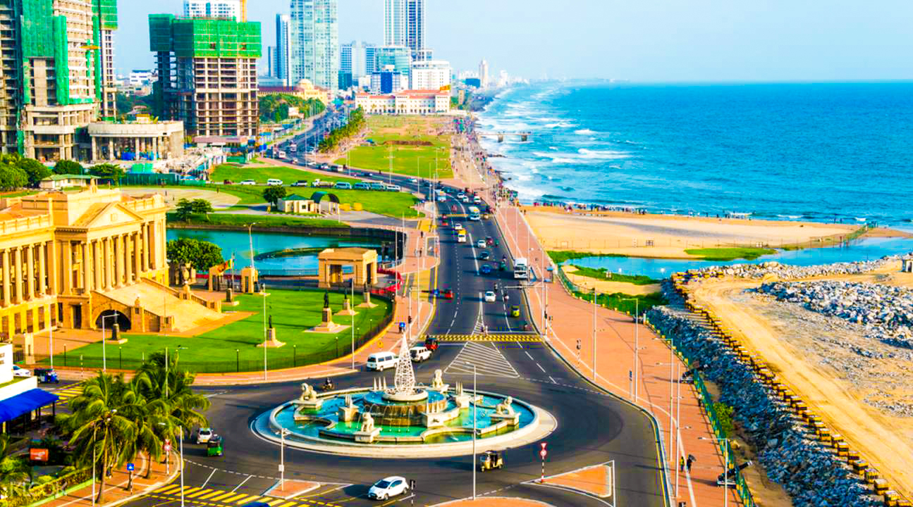 A bustling coastal city with modern buildings, a wide road, beach, and ocean under a blue sky.