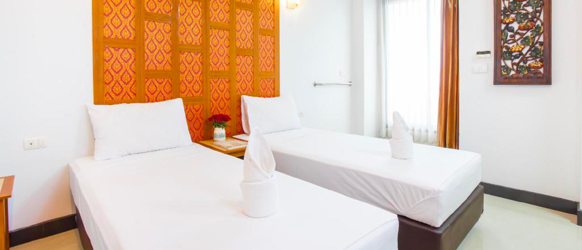 A welcoming hotel room in Bangkok featuring two single beds with white linens and traditional Thai decor.