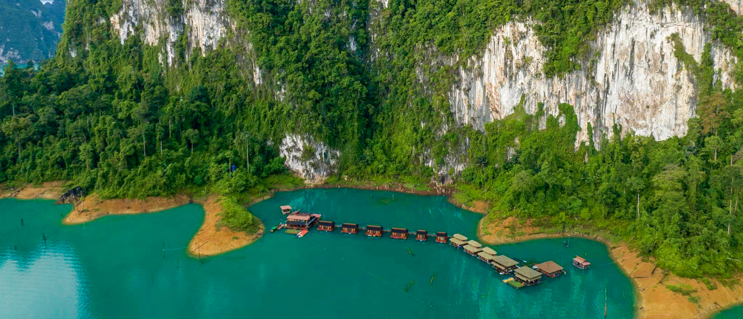Floating bungalows on a turquoise lake surrounded by lush green limestone cliffs in Thailand.
